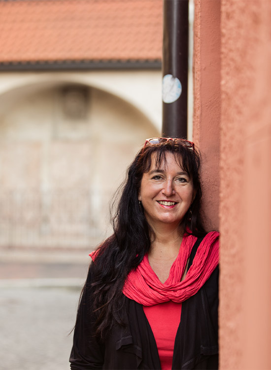 Schwarzhaarige Frau steht vor einer roten Mauer in einer Gasse in Landshut.